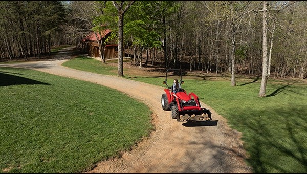 Massey Ferguson 1E Series compact tractor hauling material down a gravel driveway near a rural home in New Iberia, LA – available at USA Equipment.