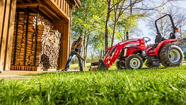 Massey Ferguson 1E Series compact tractor loading firewood beside a shed – available now at USA Equipment in New Iberia, LA.